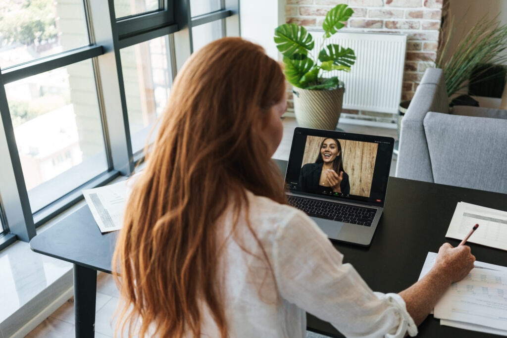 Image of redhead businesswoman making video call on laptop while sitting at table in home